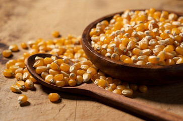 Dried corn kernels and a wooden spoon in a wooden bowl set against a wooden background.