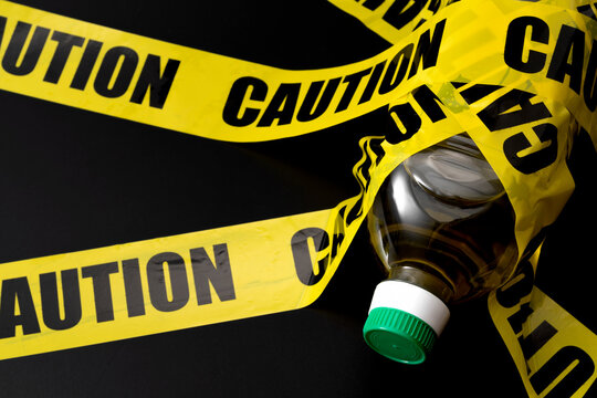 Bottle of vegetable oil (seed oils) wrapped in caution tape concept for unhealthy ultra processed foods, dietary waring for increased risk on inflammation and pro inflammatory omega six fatty acids