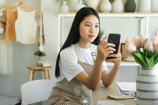 Young asian business owner holding phone and retail package parcel.