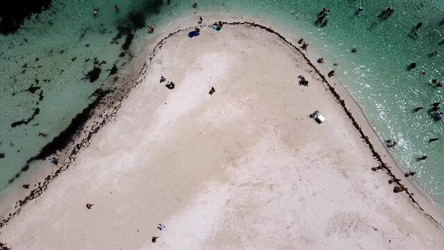 An aerial view of people walking at a beach cove in Isla Mujeres, Mexico. People are roaming on the beach and enjoying