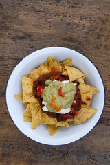 Mexican food. Top view of a white bowl with nachos, black beans pure, cream cheese and guacamole, on the wooden table.