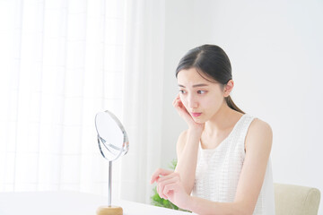 リビングで不安な表情で鏡で顔を見る女性