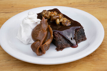 Sweet desserts. Closeup view of a bittersweet chocolate flan with vanilla cream and dulce de leche, in a white dish on the wooden table.