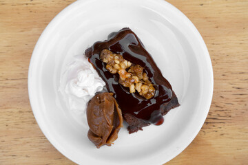 Sweet desserts. Top view of a bittersweet chocolate flan with vanilla cream and dulce de leche, in a white dish on the wooden table.