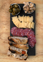Antipasto. Top view of a dish with sliced salami, cheese, focaccia peanuts and green olives on the wooden table. 