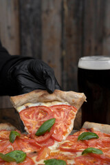 Eating pizza at the restaurant. Closeup view of the chef's hand, holding a traditional Neapolitan pizza with mozzarella cheese, sliced tomatoes, garlic and basil.