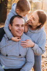 Fototapeta premium Caucasian little boy sitting on his father's shoulders being on a walk with the family in autumn park having fun. Outdoor photo in autumn park. Sunset light