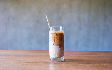 A glass of iced latte coffee with a bio straw on wooden table