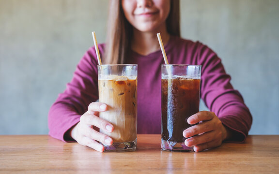 Closeup image of a young woman holding and drinking two glasses of iced coffee