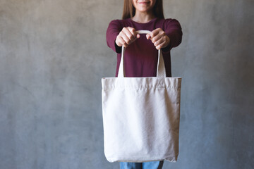 Closeup image of a young woman holding and carrying a white cloth bag for reusable and environment...