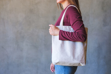 Closeup image of a young woman holding and carrying a white cloth bag for reusable and environment concept