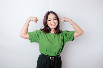 Excited Asian woman wearing a green t-shirt showing strong gesture by lifting her arms and muscles...