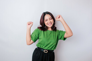 A young Asian woman with a happy successful expression wearing green shirt isolated by white...