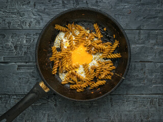 Spiral pasta and fried egg in a frying pan on a rustic background.