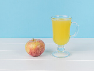 An apple and a glass of juice on a white wooden table.