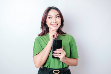 Portrait of a thoughtful young Asian woman wearing green t-shirt looking aside while holding smartphone