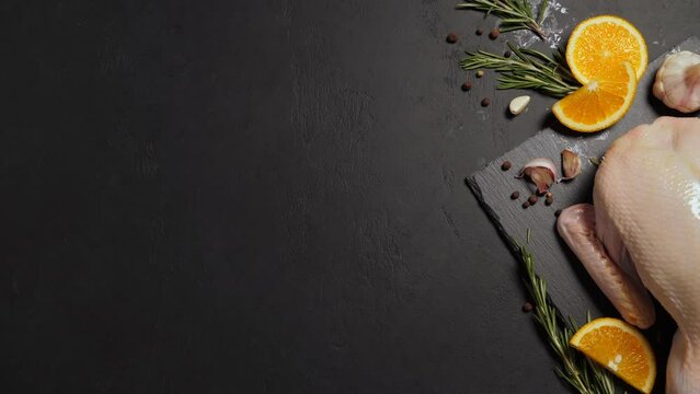 Raw organic whole duck with cut orange and rosemary on slate board on black background. Frame with copy space