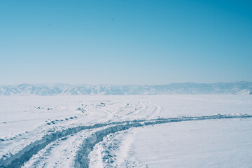Fototapeta na wymiar Wheel tracks in the snow opposite the snowy mountains.