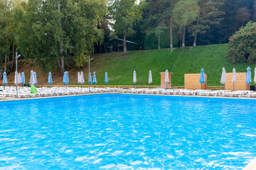 Blue pool without people on the riverbank in autumn. A great place to relax and unwind in nature. The pool and sun beds are waiting for visitors
