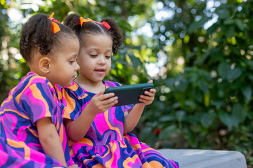 twin sisters children girls using cell phone smartphone outdoors happy