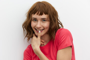 Fototapeta premium photo of a mischievous, cheerful, pleasant woman with red hair standing on a white background with an empty space for inserting an advertising layout and playfully holding a finger near her mouth