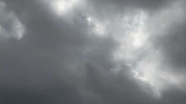 Close up static time-lapse thick white grey clouds pass across sky left to right with sun flare through clouds peaks.