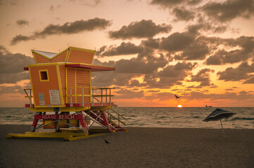Sunrise in Miami Beach.  Horizontal.  Life guard tower, birds, umbrella and boat over an orange sunrise. 