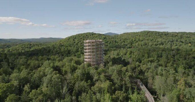 Beautiful wooden tower hiking trail. Mountains and trees. Marvelous sunny summer day. 4k drone circling structure. Mid far point of view. Ski resort in the background. Professional pilot.