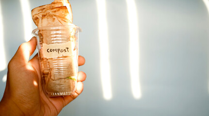 Close up of hand holding plastic drinking glass full of used teabag with text compost written on...
