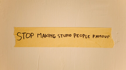 word text of stop making stupid people famous written on duct tape isolated on dirty white wall....