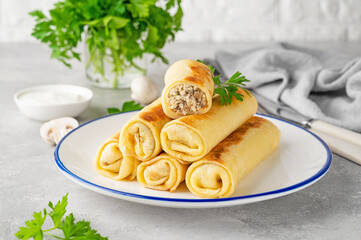Pancakes or thin crepes stuffed with chicken and mushrooms on a plate on a gray concrete background. Selective focus, copy space.
