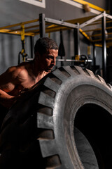 Fototapeta na wymiar High quality photo. Very muscular man, you can see the vein when making an effort. Latin man pushing a giant tire. Hispanic man training in a gym with a tire.
