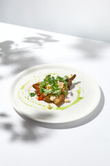 Baked eggplant with cheese on white table with harsh shadows. Aesthetic italian food - baked aubergine on white plate. Stuffed eggplant in minimal style. Stuffed aubergine in vegan menu.