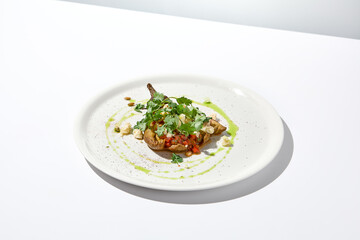 Baked eggplant with cheese on white table with harsh shadows. Aesthetic italian food - baked aubergine on white plate. Stuffed eggplant in minimal style. Stuffed aubergine in vegan menu.