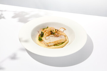 Roasted squid on mashed potatoes and crispy onion. Grilled squid with celery cream on white plate with shadows of leaves. Summer seafood menu. Roasted calamari in fine dining.