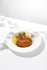 Traditional italian dish - osso buco with risotto milanese. Stew meat on bone with rice on white plate. Summer italian dining. Italian osso buco with garnish with hard shadows