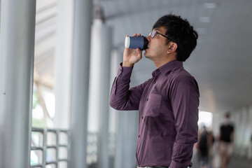 Young Asian businessman standing drinking acup of coffee​ and look ahead. Copy​ space on the right
