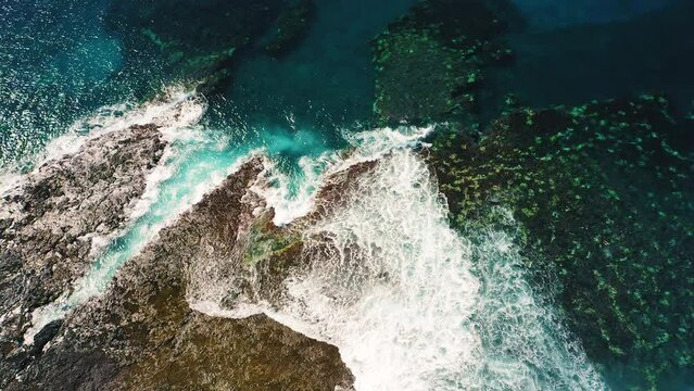 Colorful waters of the ocean, swirl around the rocky and scenic coastline. Sea waves breaking over rocks. Azure blue transparent clear aqua. White foam. Picturesque landscape. Aerial.
