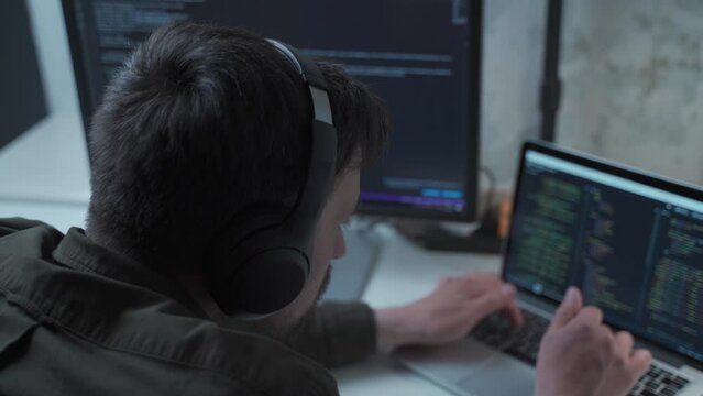 Caucasian man in headphones IT coder programmer software engineer use laptop computer typing code develop program programming java language application on screen web system app development concept.
