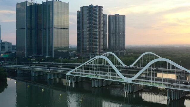 traffic crossing a bridge in PIK area of Jakarta with modern high-rise buildings at sunset, aerial