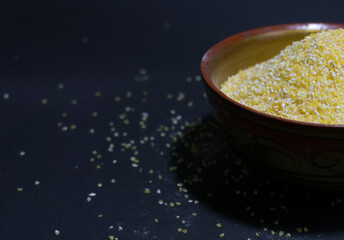 Raw corn grits in a wooden bowl on a black background