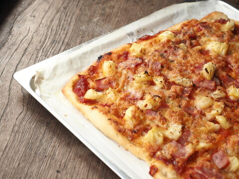 rectangle shaped Hawaiian pizza in baking tray on wood