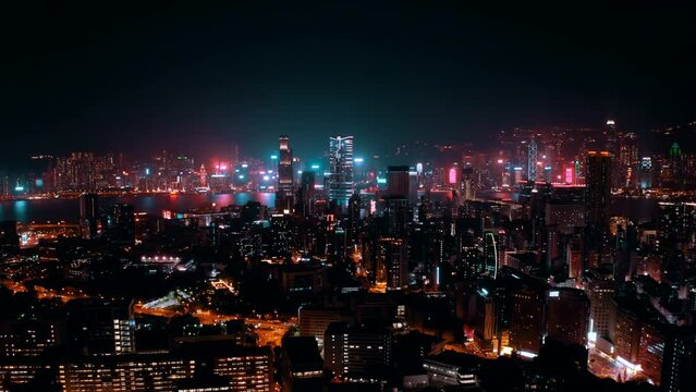 Drone shot, traveling to the right, of the city of Hong Kong during the night with many business buildings in the distance. The streets are busy and give the shot a cyberpunk atmosphere.