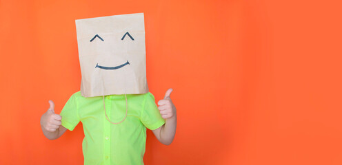 A child with a paper bag on his head in the form of a smiley face shows with two hands gesture of 