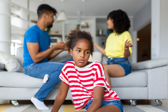 Divorce And Domestic Violence. Portrait of upset African American daughter looking through the window while her angry parents fighting in the background, depressed child feeling lonely