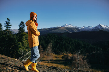 Woman full-length hiker standing frozen on the mountain looking at nature happiness with a view of the mountains in a yellow raincoat travel and hiking in the mountains at sunset freedom