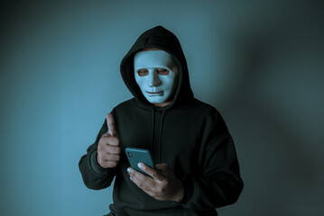 An anonymous masked hacker is using a smartphone to penetrate credit card financial information....