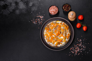 Delicious fresh liver cake with mayonnaise and carrots on a black plate against a dark concrete background
