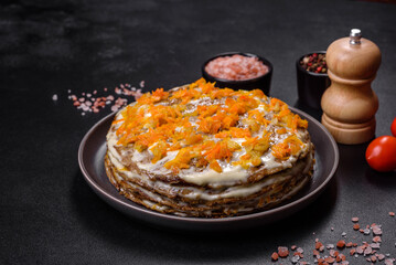 Delicious fresh liver cake with mayonnaise and carrots on a black plate against a dark concrete background