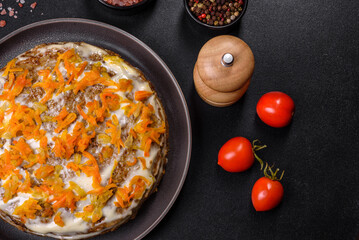 Delicious fresh liver cake with mayonnaise and carrots on a black plate against a dark concrete background
